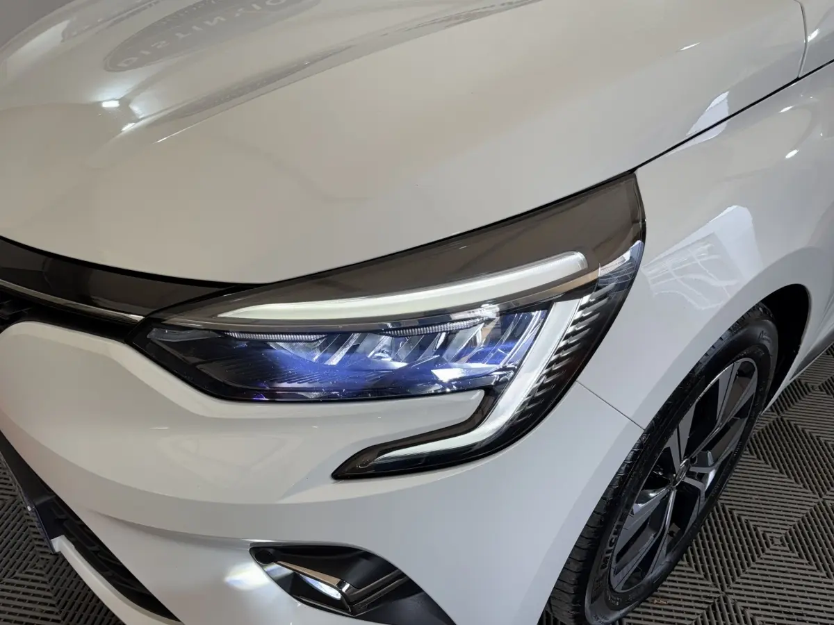 Gros plan sur le phare avant droit LED et la roue alliage noire d'une Renault Clio Business blanche 2023.