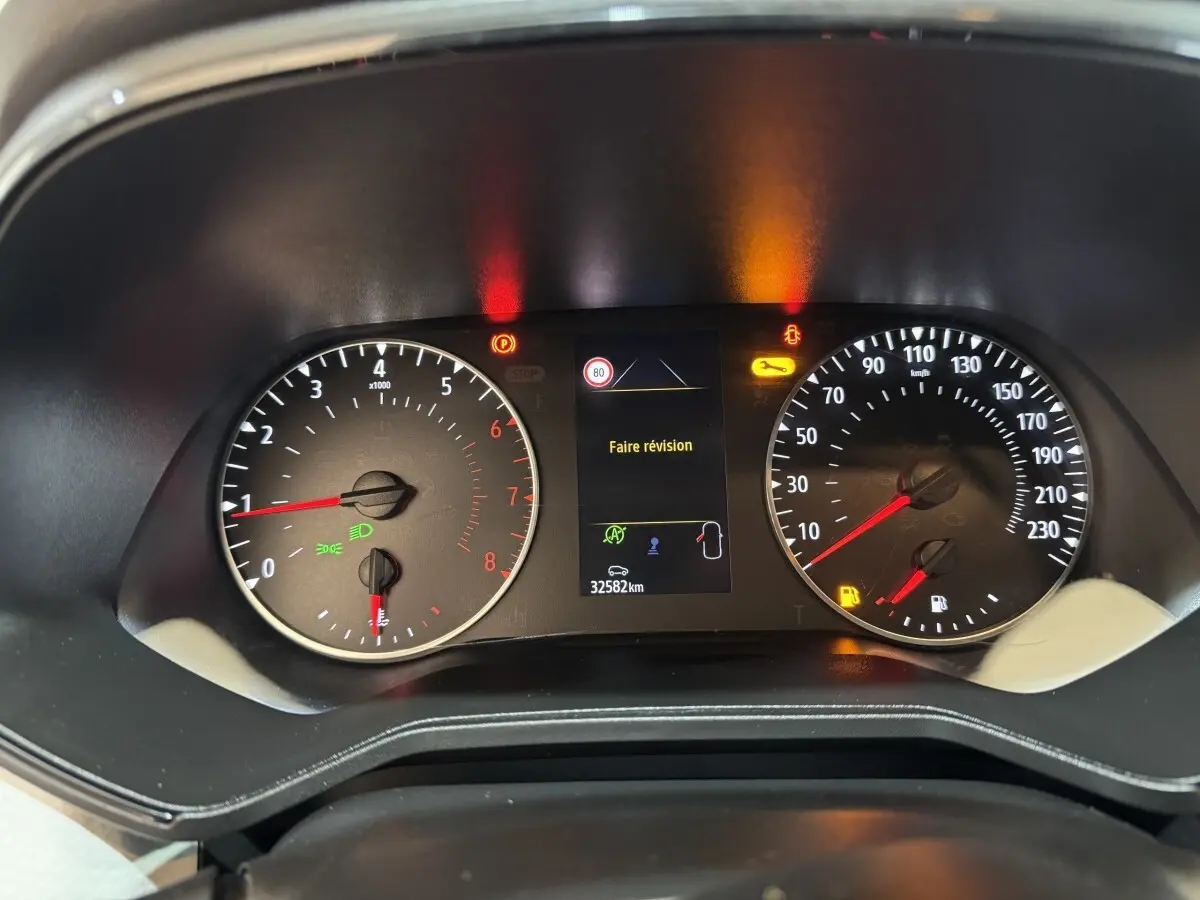 Vue rapprochée du tableau de bord de la Renault Clio blanc 2023, affichant un message "Faire révision" et compteurs analogiques.