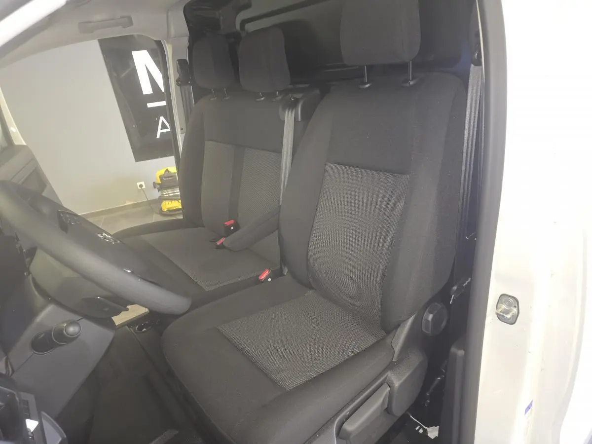 Vue intérieure côté conducteur de l'Opel Vivaro blanc 2025, sièges tissu bi-ton noir et gris avec appuie-têtes.