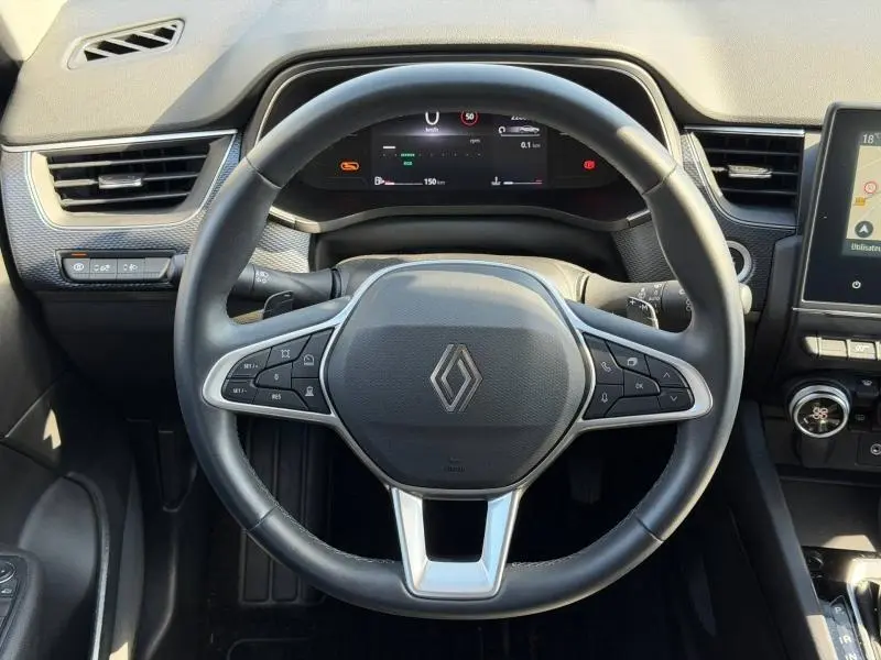 Vue rapprochée du volant multifonction noir avec logo Renault au centre, tableau de bord digital et partie de la console centrale.