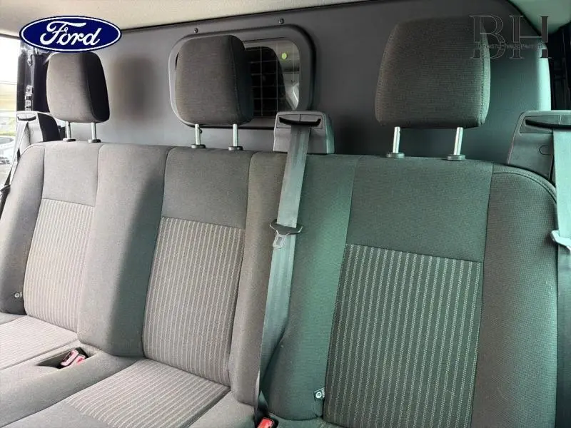 Vue intérieure sur la banquette arrière tissu gris du Ford Transit Custom Fourgon noir avec cloison vitrée en arrière-plan.