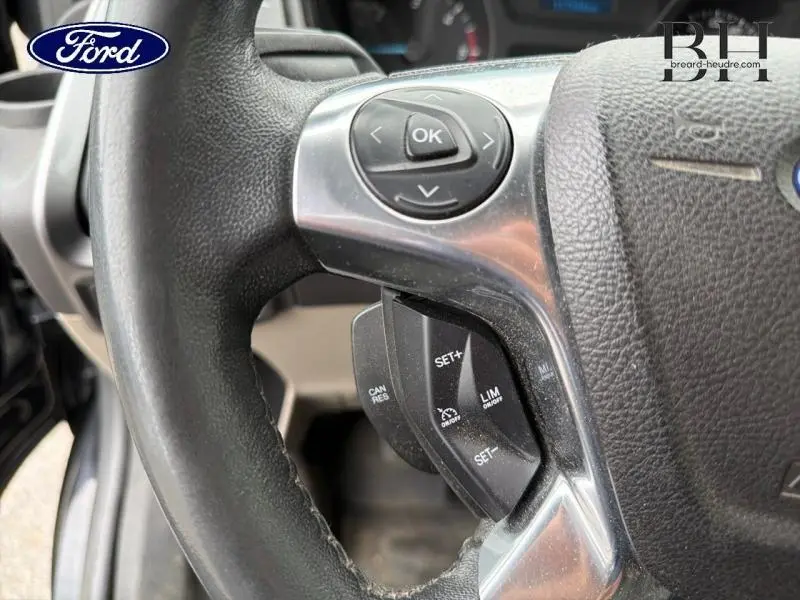 Gros plan sur les commandes au volant cuir noir du Ford Transit Custom Fourgon 2013, avec boutons multifonctions visibles.