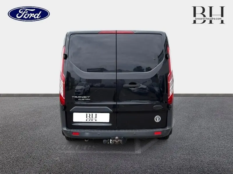Vue arrière d'un fourgon Ford Transit Custom noir avec double portes et attelage de remorque visible.