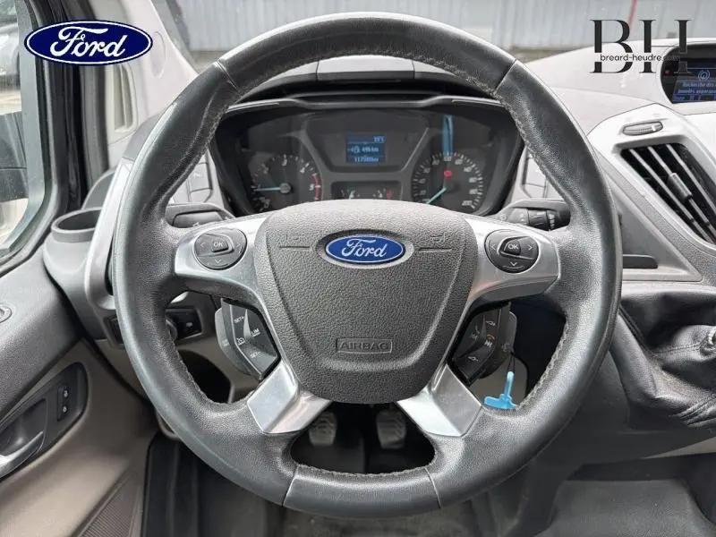 Vue rapprochée du volant cuir noir du Ford Transit Custom Fourgon 2013 avec commandes audio intégrées.
