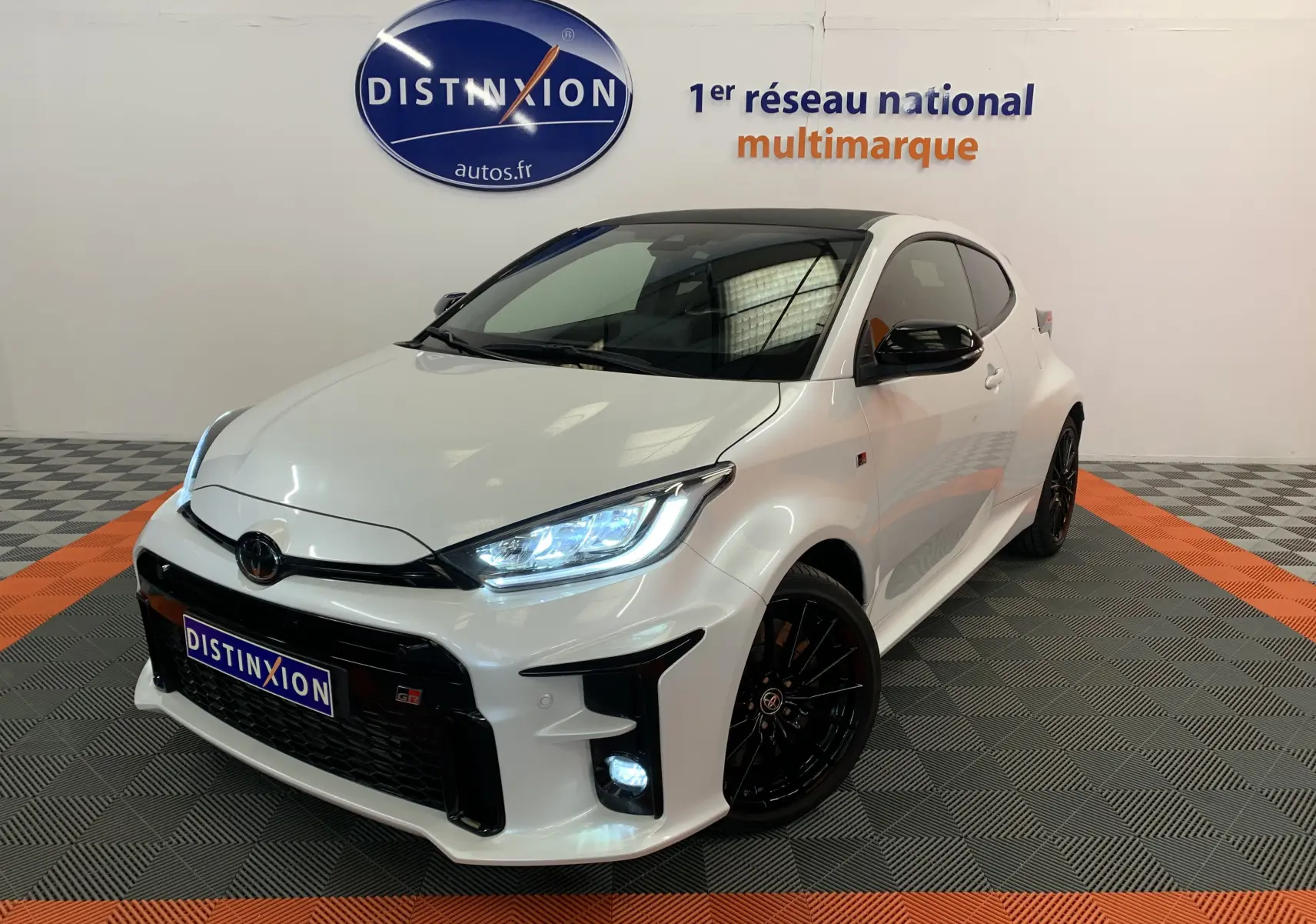 Toyota Yaris 1.6 VVT-I 261 Premium GR blanc métal vue 3/4 avant avec phares LED allumés et jantes noires.