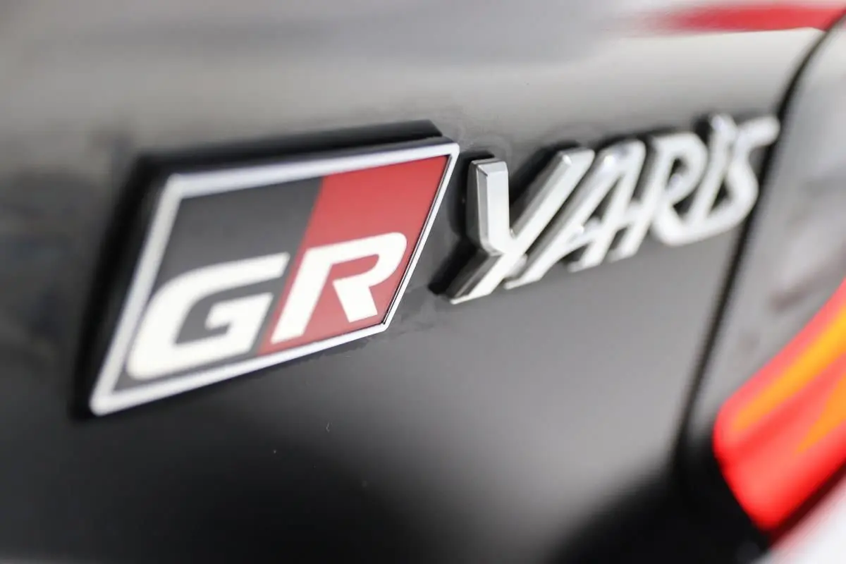 Gros plan sur l'emblème GR et le logo Yaris sur une carrosserie noire avec un détail rouge vif.