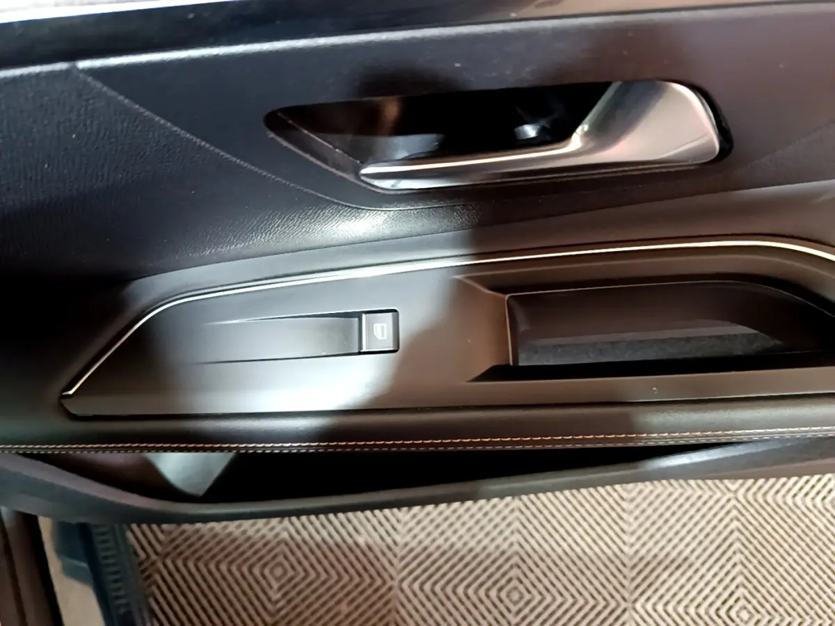 Gros plan sur la poignée intérieure et le bouton de lève-vitre côté gauche d’une Peugeot 3008 GT bleu.