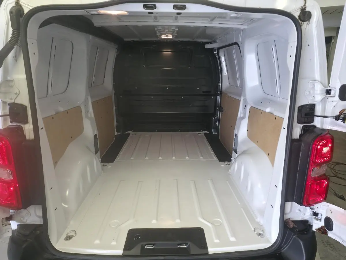 Vue arrière intérieure du fourgon Opel Vivaro blanc 2025, montrant l'espace de chargement vide avec panneaux latéraux en bois.