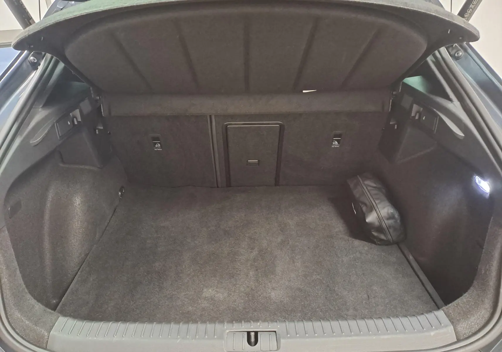 Coffre ouvert de la CUPRA Formentor gris magnétique 2024, montrant un espace de chargement propre avec une trappe centrale et une petite trousse noire.