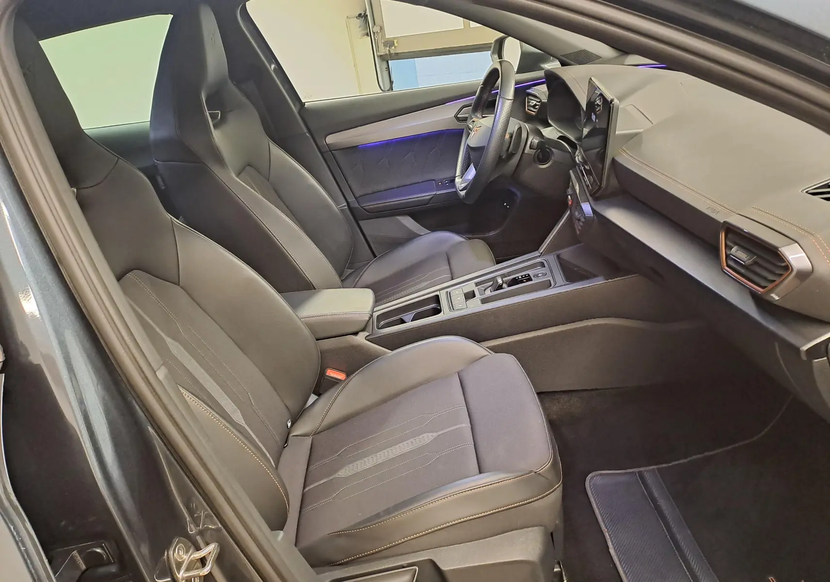Vue intérieure côté conducteur du CUPRA Formentor 1.4 e-HYBRID 245 DSG6 VZ 2024 avec sièges noirs et éclairage d'ambiance violet.