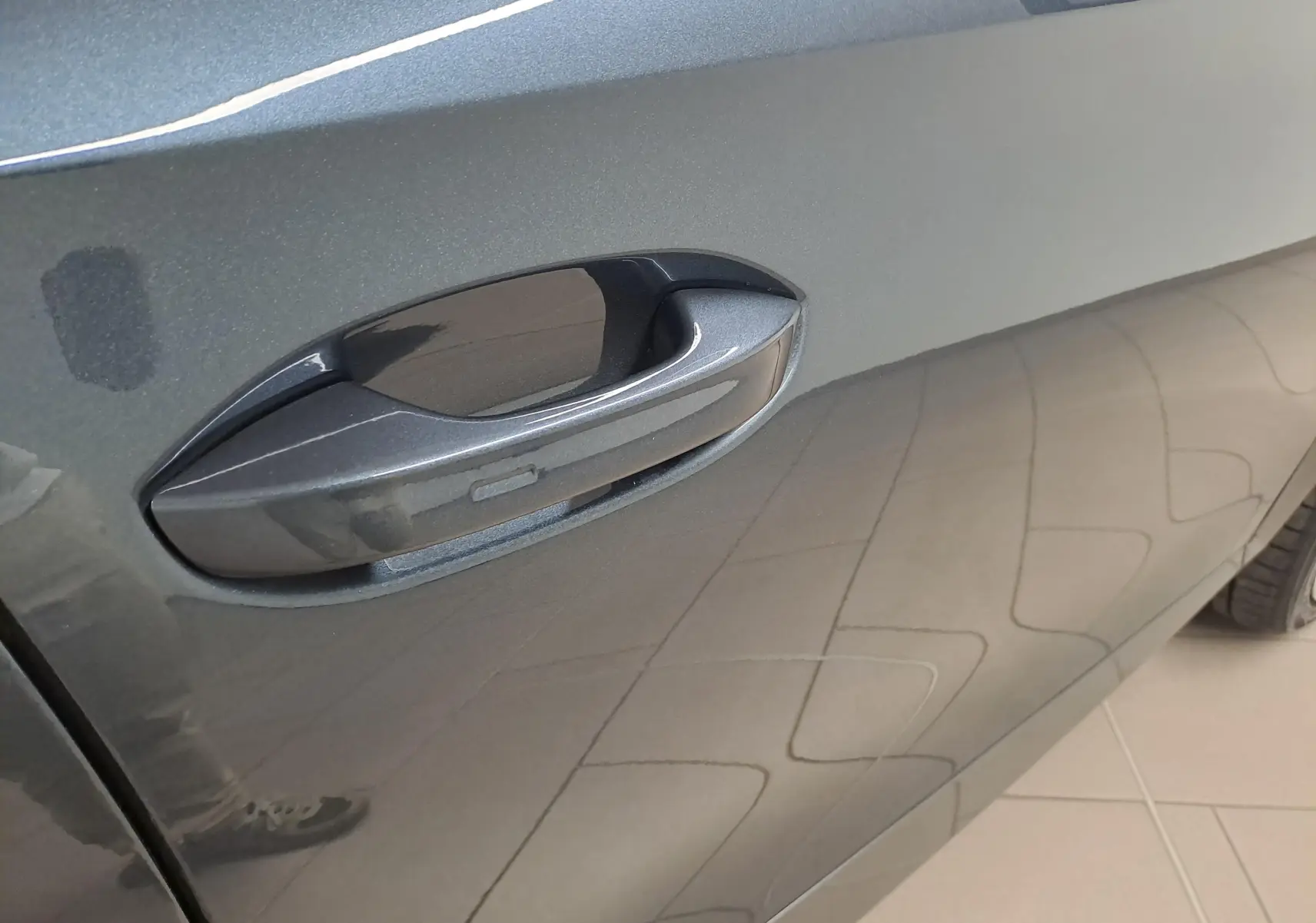 Poignée de porte côté gauche de la CUPRA Formentor 1.4 e-HYBRID 245 gris magnétique avec reflet du sol carrelé.