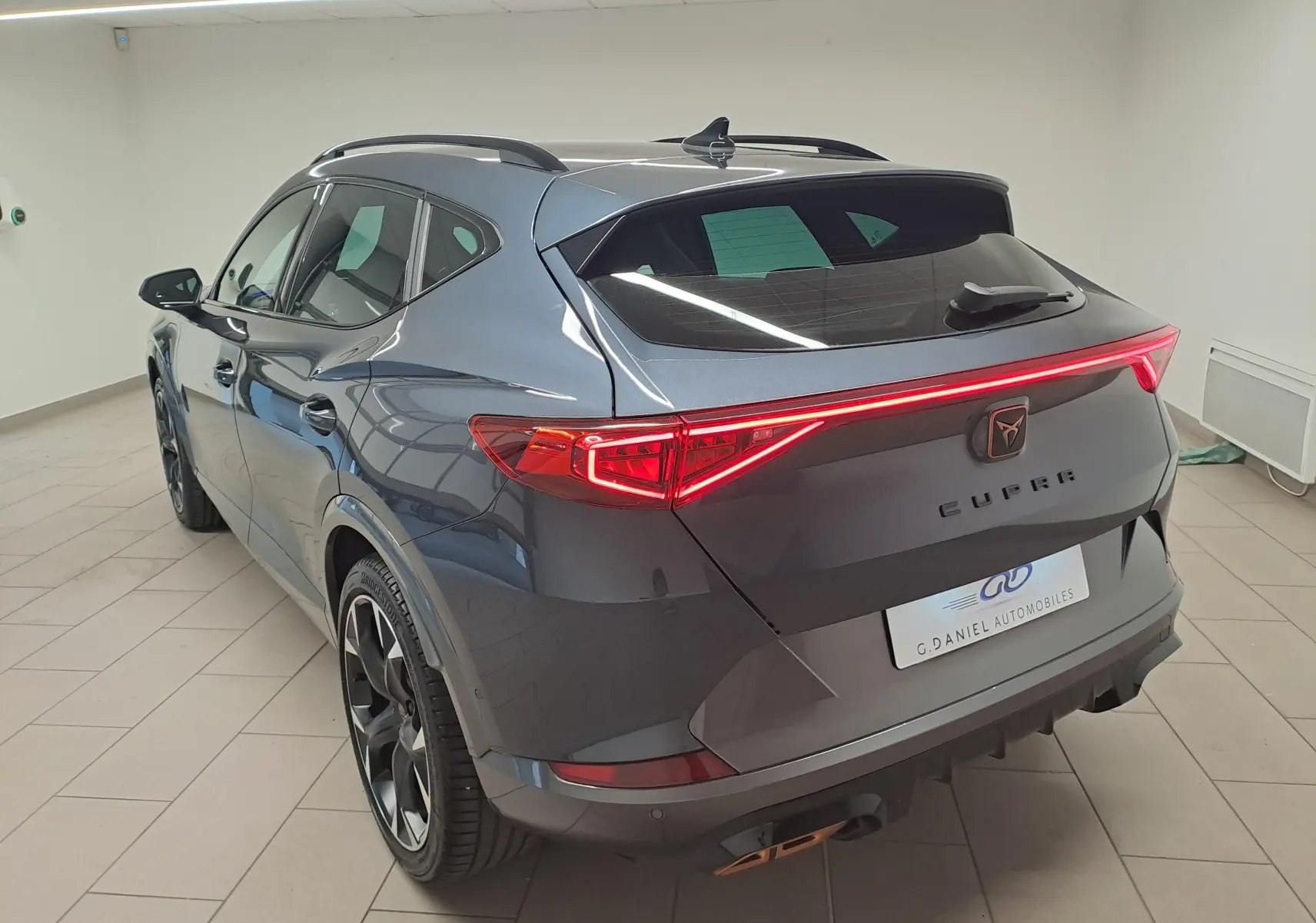 Vue 3/4 arrière droite du CUPRA Formentor 1.4 e-HYBRID 245 gris magnétique avec feux arrière allumés en intérieur.