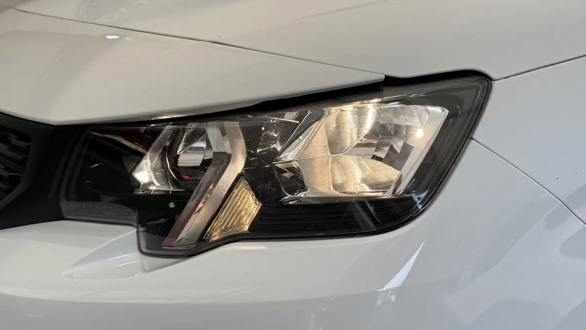 Gros plan sur le phare avant droit du Peugeot Partner blanc, mettant en valeur son design moderne et précis.