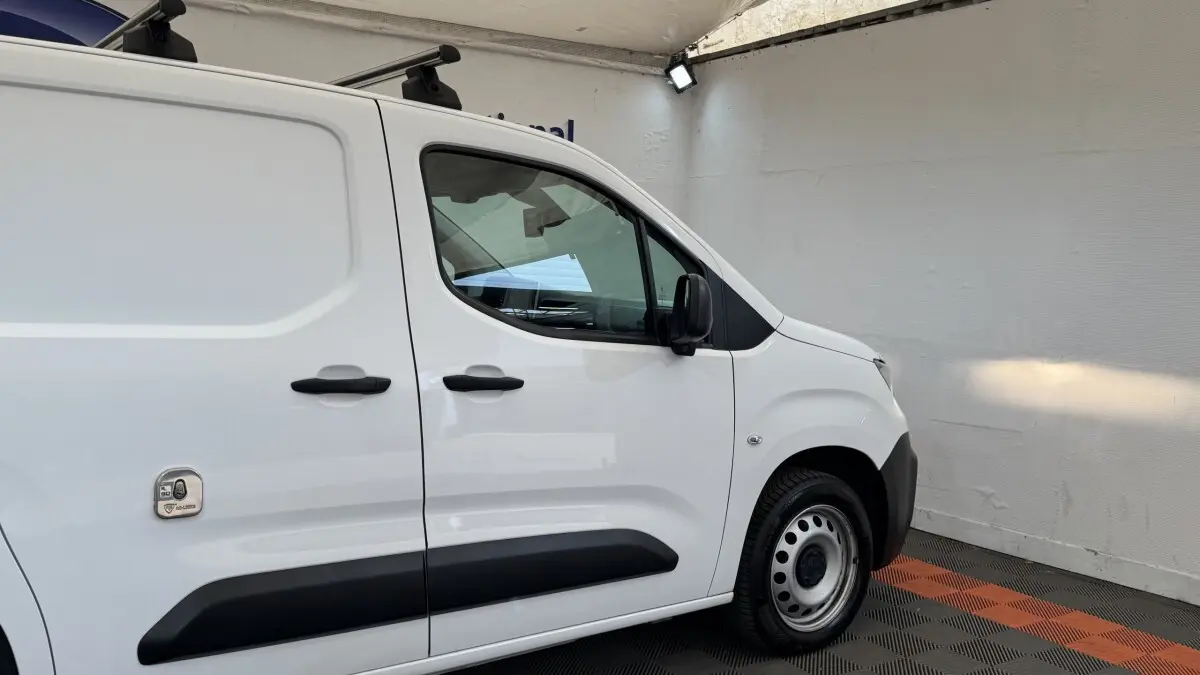 Vue de profil côté droit du Peugeot Partner blanc utilitaire avec protections noires et toit équipé de barres.