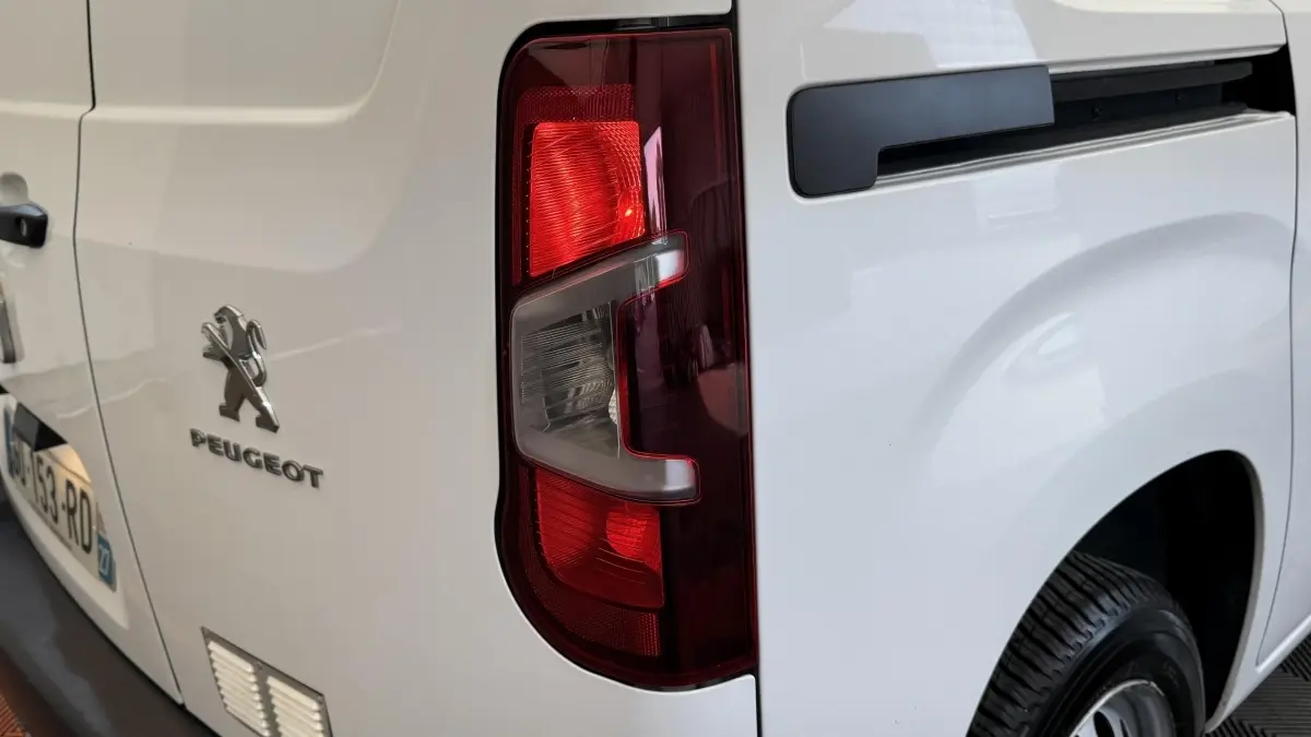 Gros plan sur le feu arrière droit d’un Peugeot Partner blanc, avec logo et partie de la porte arrière visible.