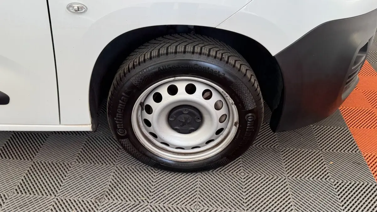 Gros plan sur la roue avant droite en jante acier du Peugeot Partner blanc, avec partie basse de la carrosserie visible.