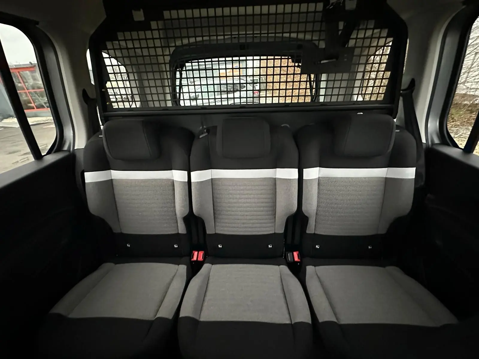 Vue intérieure arrière du Citroën Berlingo gris Artense, montrant les trois sièges arrière avec grille de séparation.