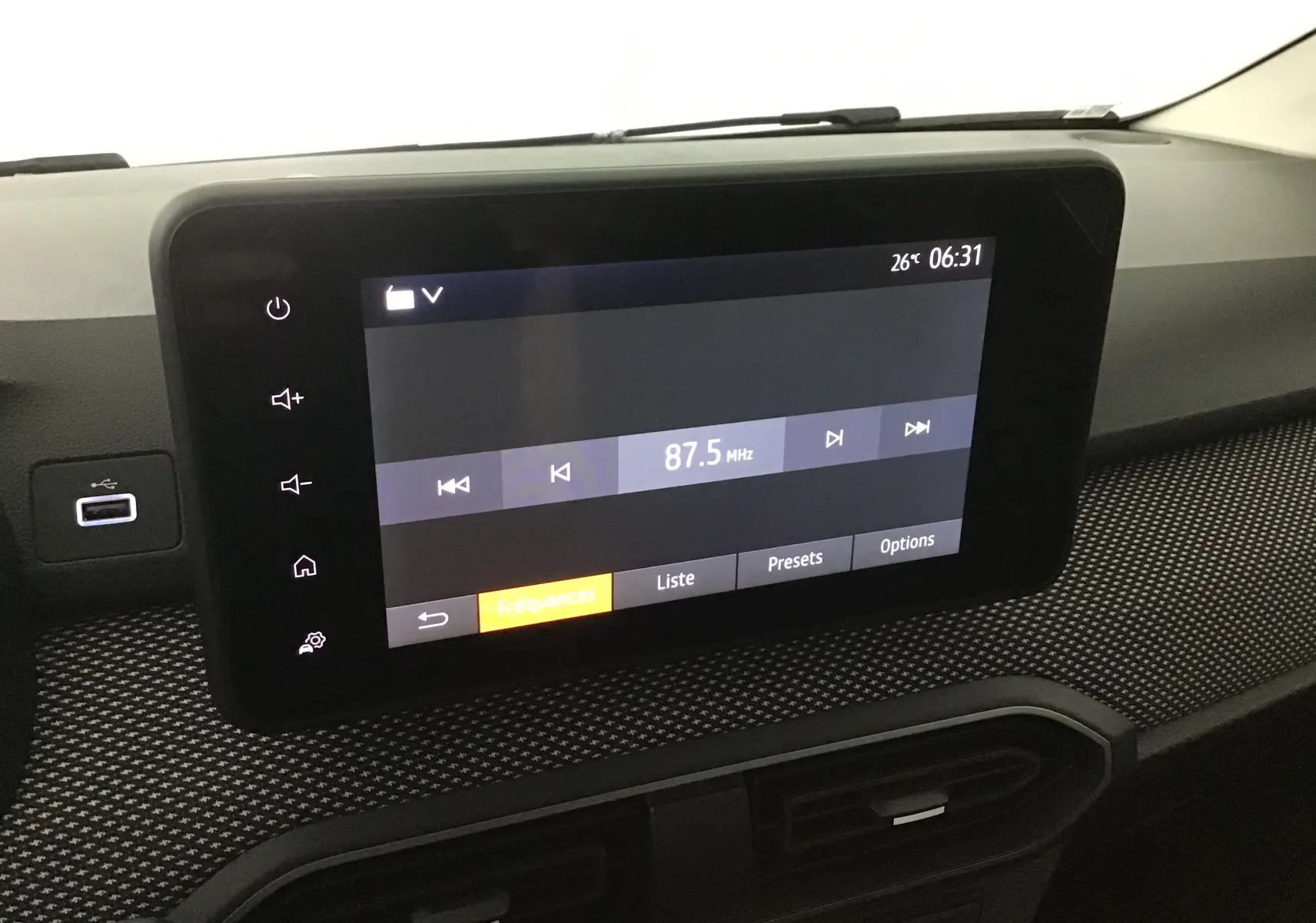 Écran tactile central de la Dacia Sandero Stepway 2025 affichant la radio FM à 87,5 MHz sur un tableau de bord texturé.
