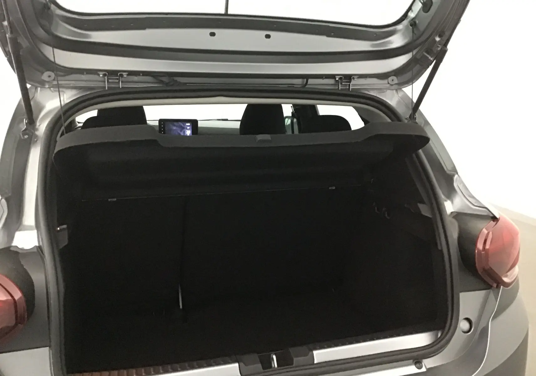 Coffre ouvert vu de l'arrière droit d'une Dacia Sandero Stepway gris schiste, intérieur sombre et tablette visible.