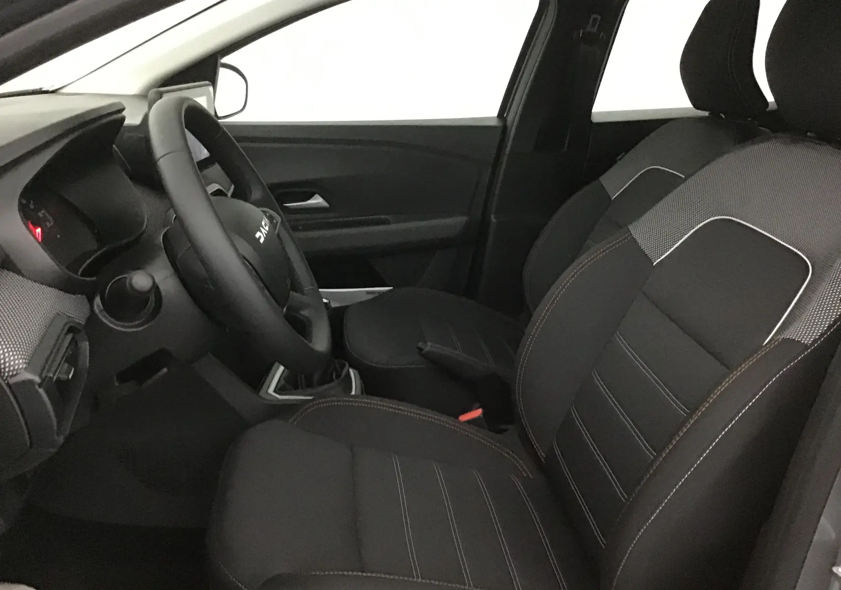 Intérieur côté conducteur de la Dacia Sandero Stepway 2025, montrant les sièges noirs avec surpiqûres et volant multifonction.