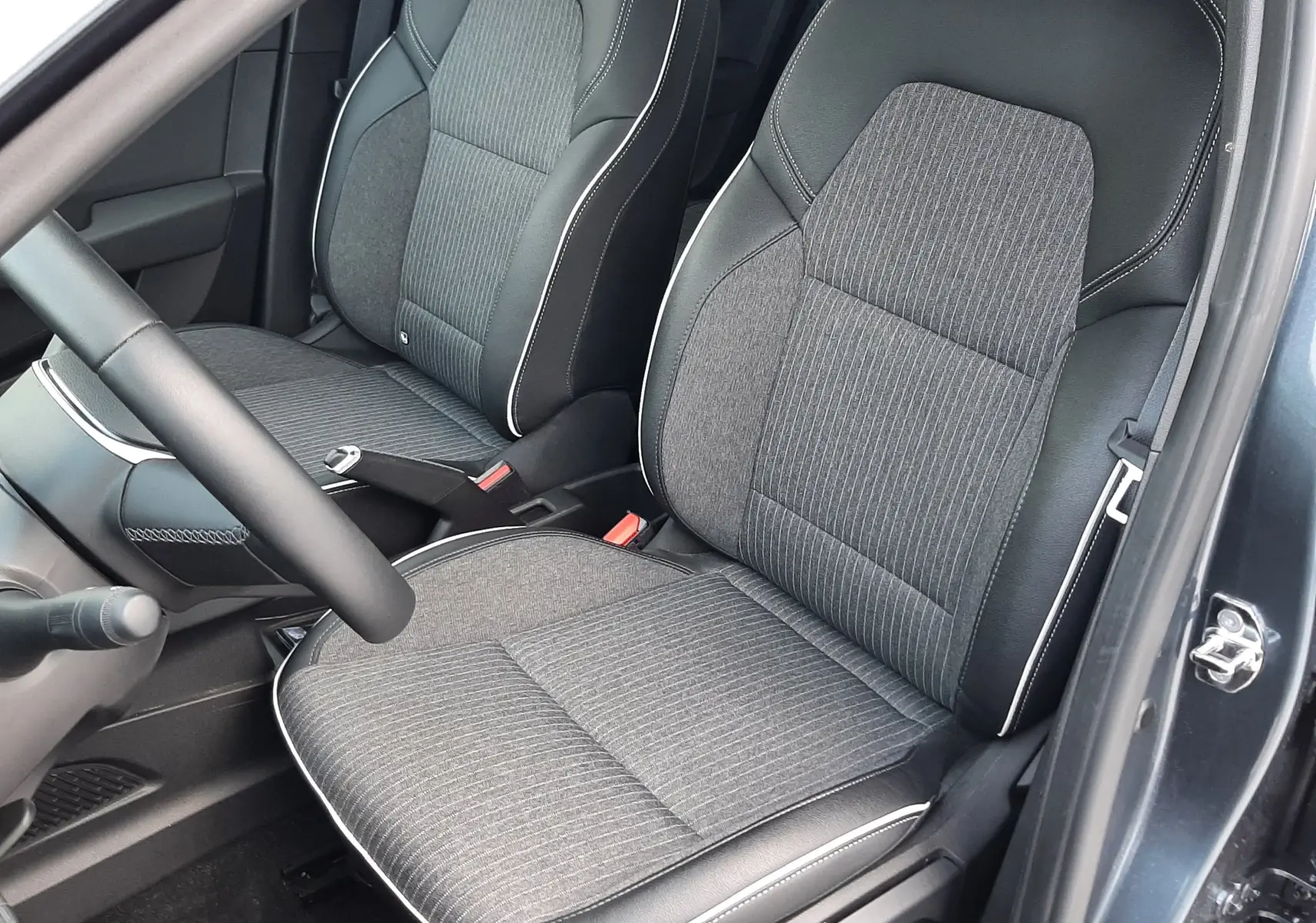 Vue intérieure côté conducteur de la Renault Clio V TCE 90 Intens avec sièges tissu gris et surpiqûres blanches.