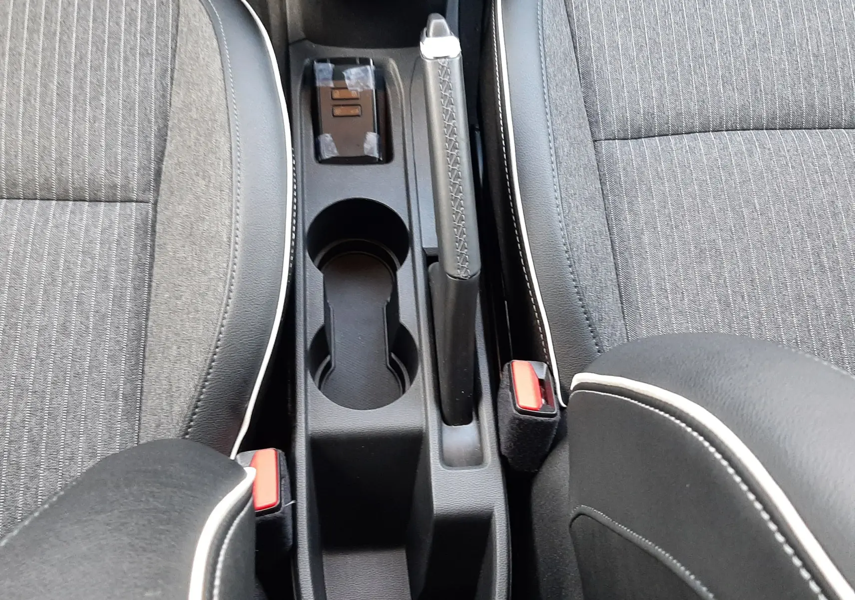 Vue plongeante sur la console centrale et les sièges gris tissu avec surpiqûres blanches d'une Renault Clio V 2021.