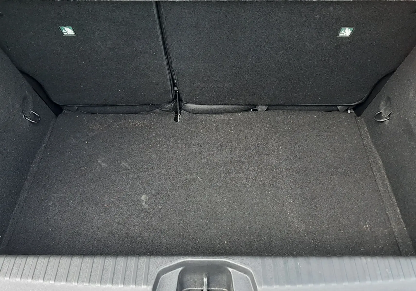 Coffre vide vu de dessus de la Renault Clio V gris titanium, montrant la moquette noire et les dossiers arrière rabattus.