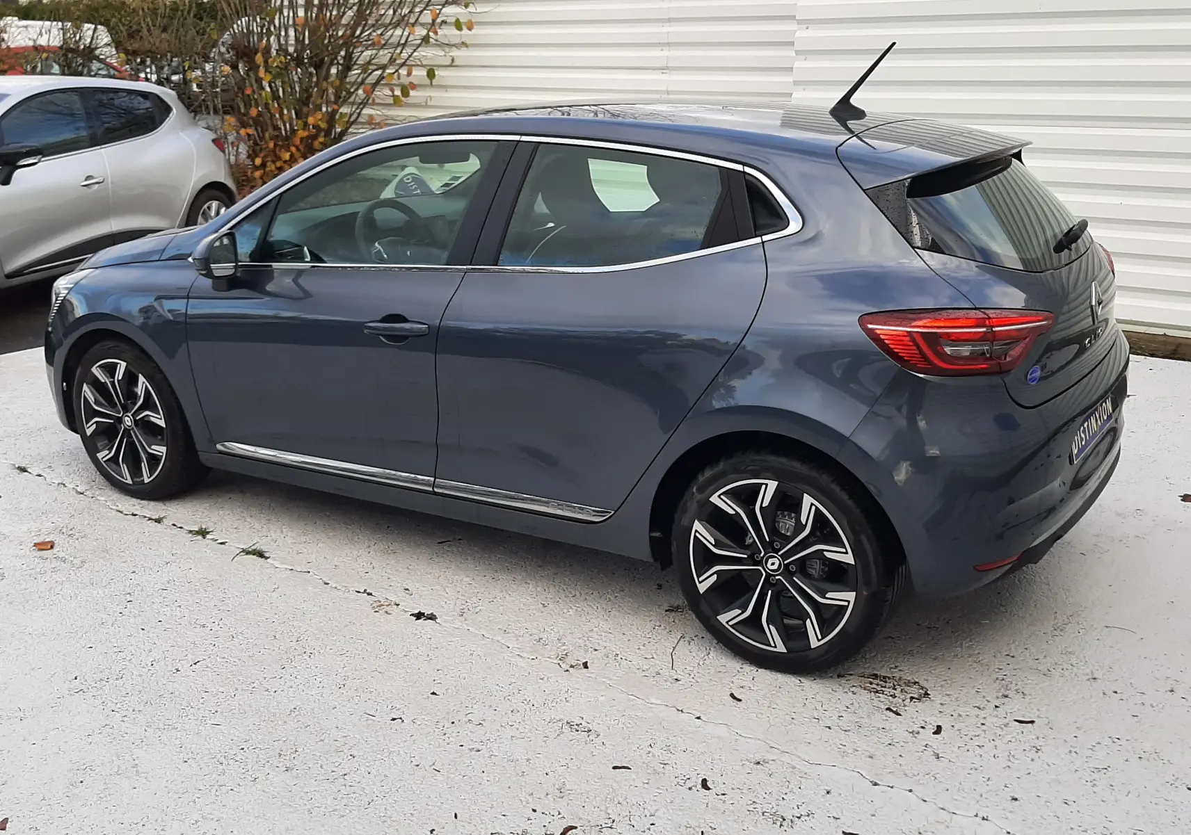 Renault Clio V gris titanium vue de profil côté gauche, avec jantes alliage noires et chromées, en extérieur.