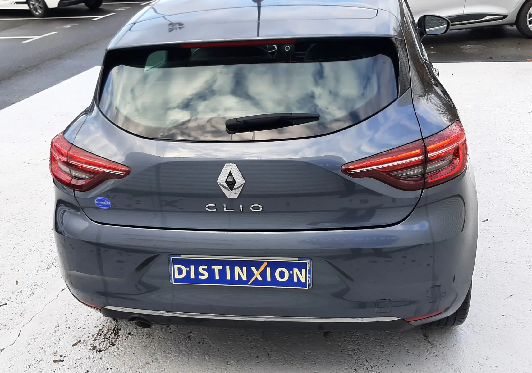Vue arrière d'une Renault Clio V gris titanium, avec feux arrière LED et plaque d'immatriculation Distinxion visible.