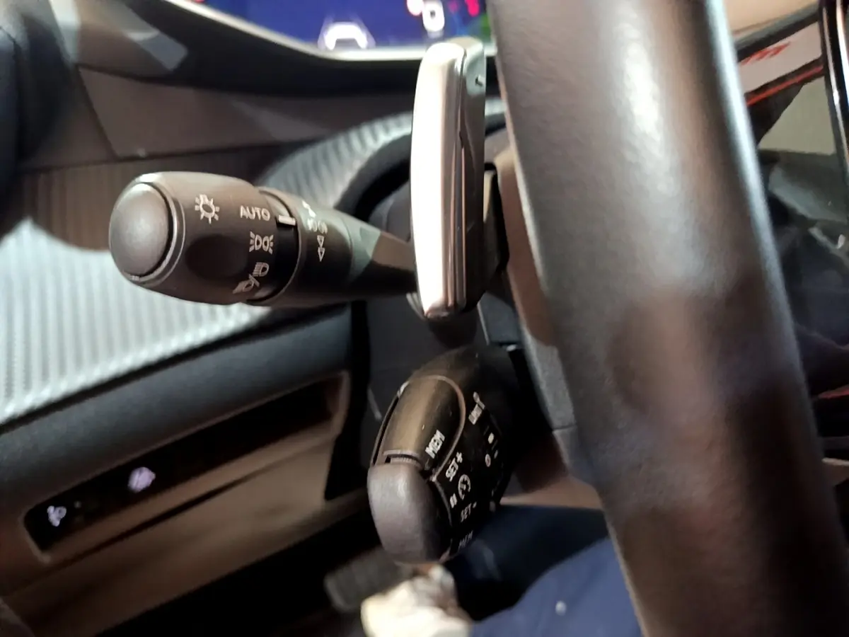 Gros plan sur les commandes au volant côté gauche du Peugeot 2008 orange, montrant les leviers de feux et régulateur de vitesse.