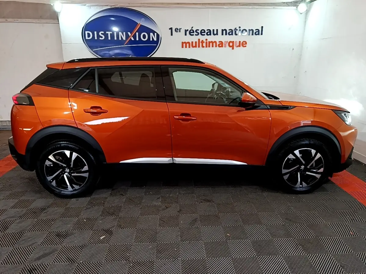 Vue de profil côté gauche d’un Peugeot 2008 orange avec jantes noires et toit noir dans un showroom.