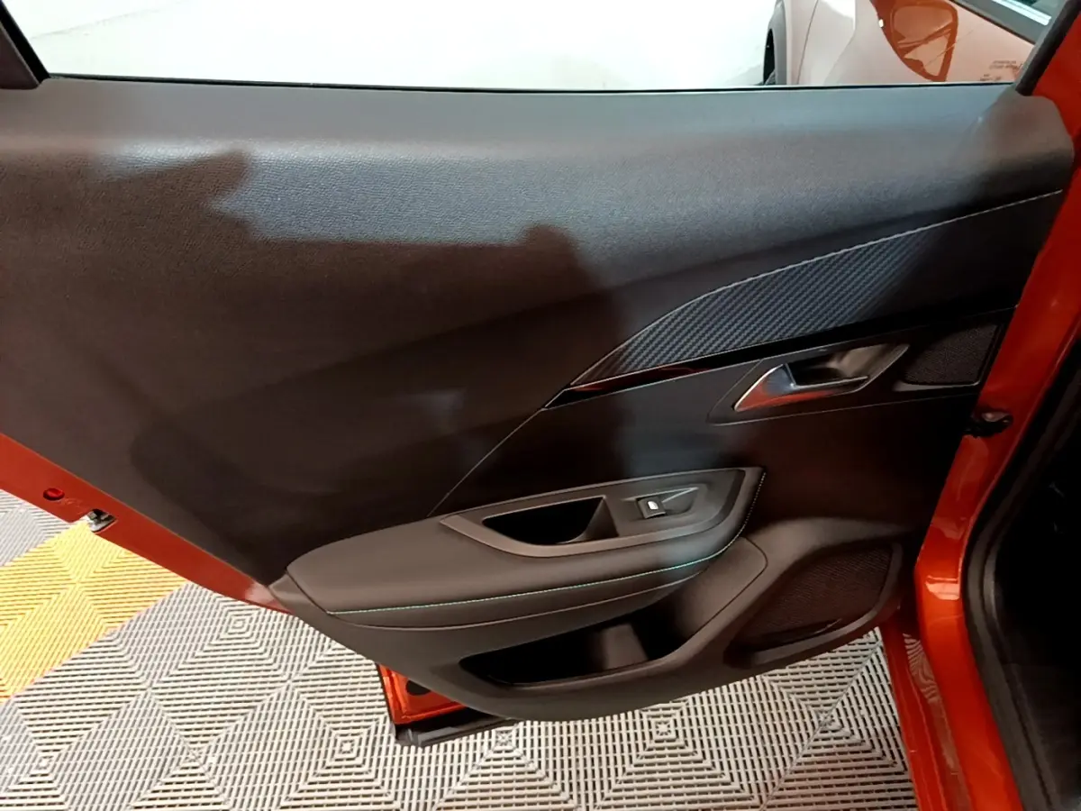 Vue rapprochée de la porte avant gauche orange du Peugeot 2008 2021, mettant en valeur les finitions intérieures noires et le bouton de lève-vitre.