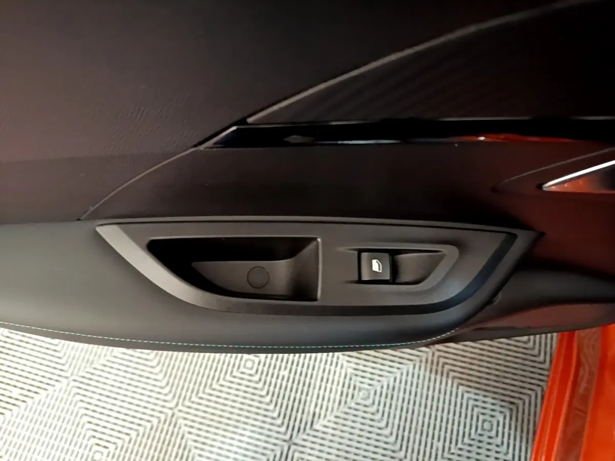 Gros plan sur la poignée intérieure et bouton de verrouillage de la porte côté gauche d’un Peugeot 2008 orange.