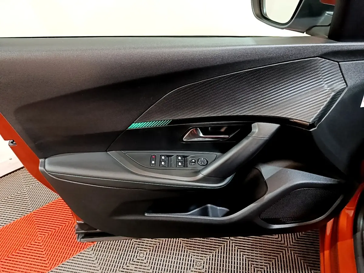 Vue intérieure de la porte avant gauche d'une Peugeot 2008 orange, avec commandes électriques et insert décor carbone.