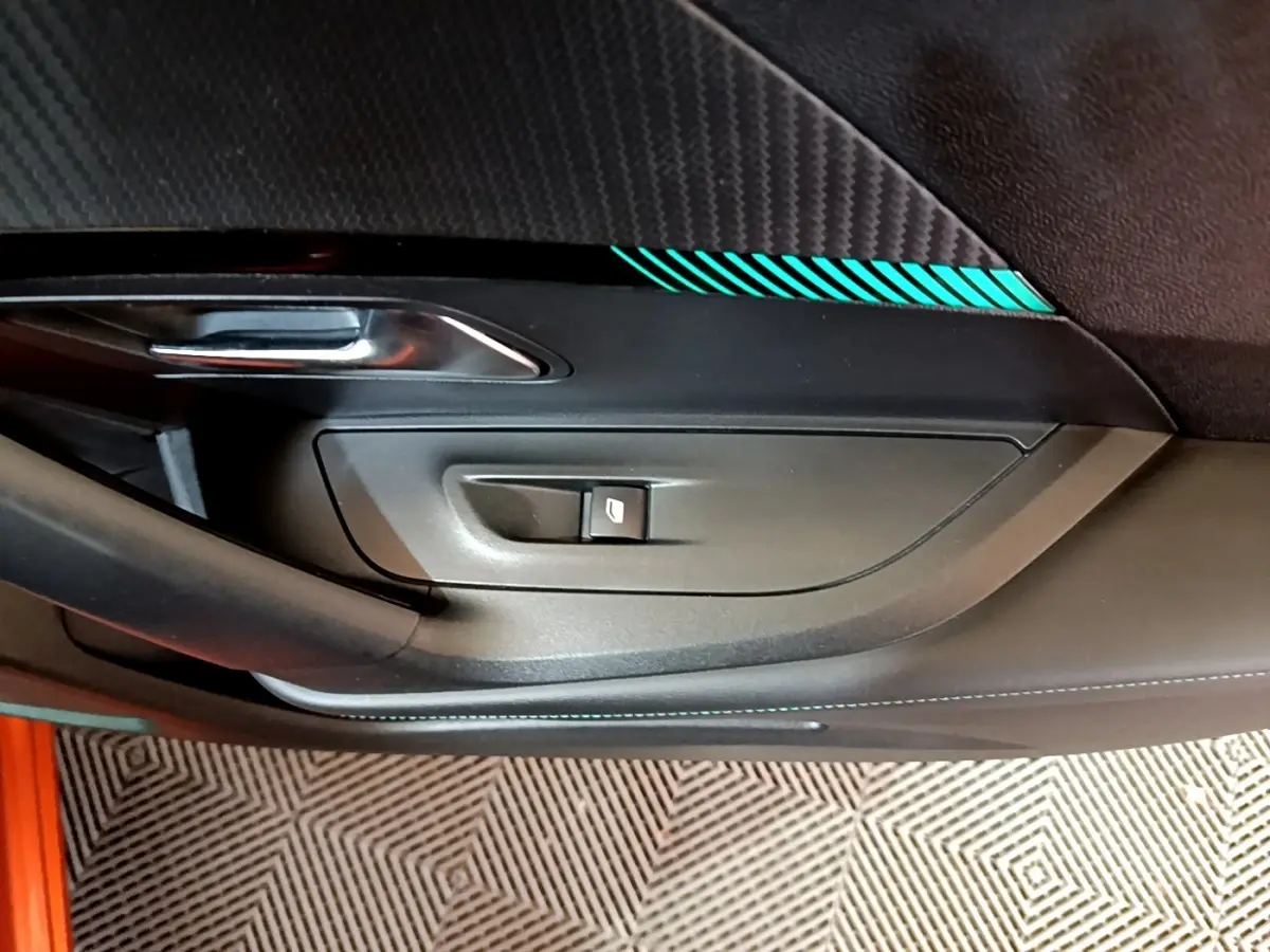 Gros plan sur la portière intérieure côté conducteur d’une Peugeot 2008 orange avec surpiqûres turquoise et bouton de lève-vitre.