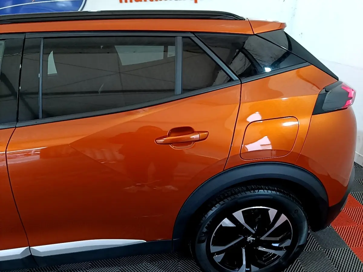 Vue latérale droite sur l’arrière d’un Peugeot 2008 orange métallisé avec jante noire et toit noir contrasté.