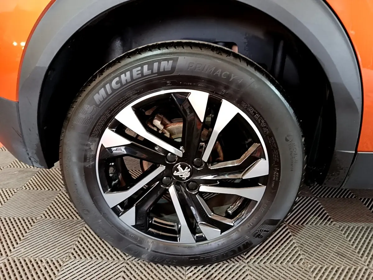 Gros plan sur la roue avant droite d’un Peugeot 2008 orange, jante alliage noire et argent avec pneu Michelin.
