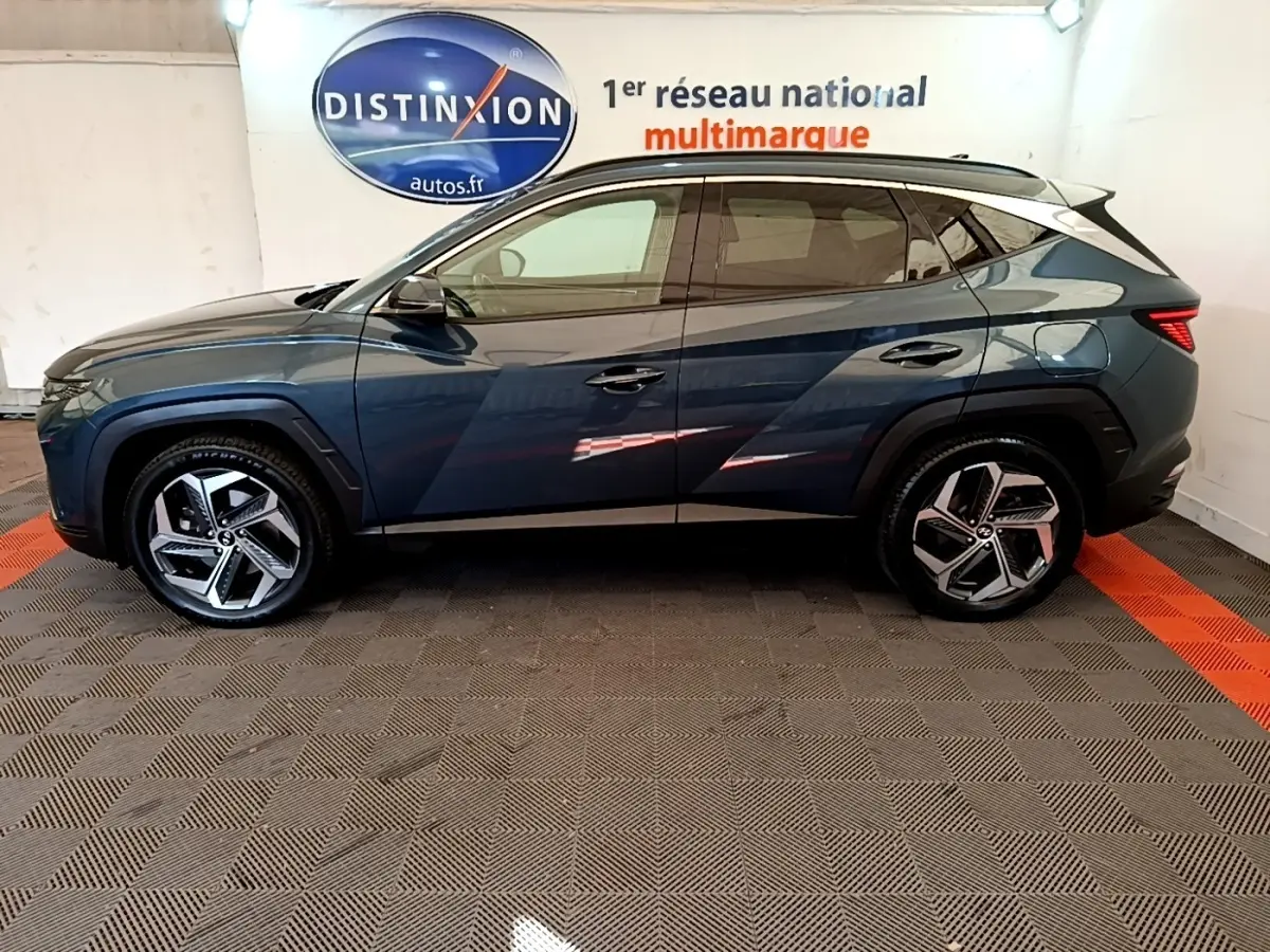 Vue de profil côté gauche du Hyundai Tucson bleu 2023 avec jantes alliage et toit noir contrasté.