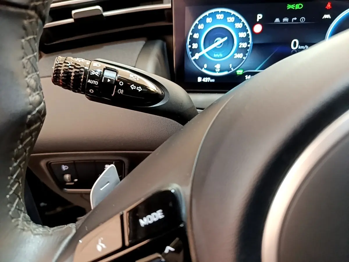 Gros plan sur le volant et la manette de clignotant du Hyundai Tucson bleu, avec tableau de bord numérique allumé en arrière-plan.