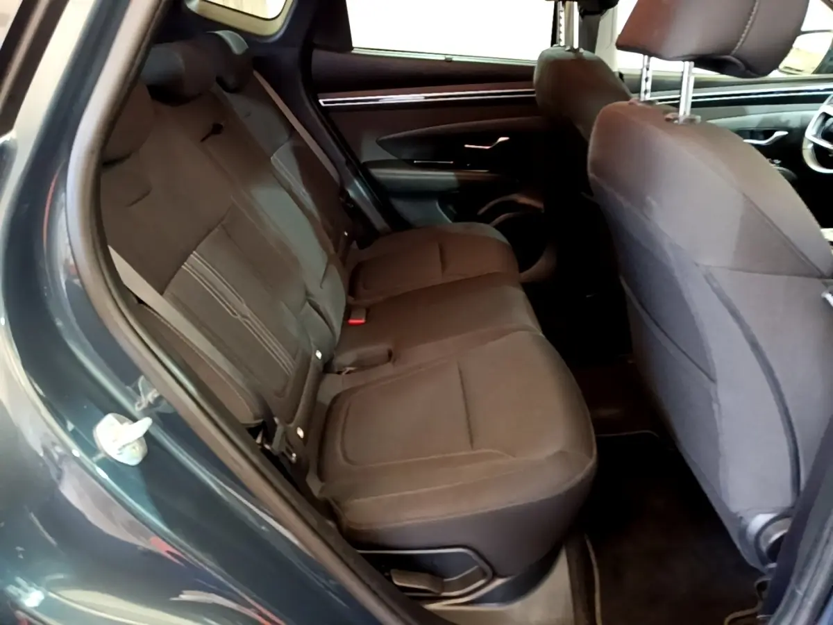 Vue intérieure côté gauche sur les sièges arrière noirs du Hyundai Tucson bleu, avec partie avant et porte ouverte visible.