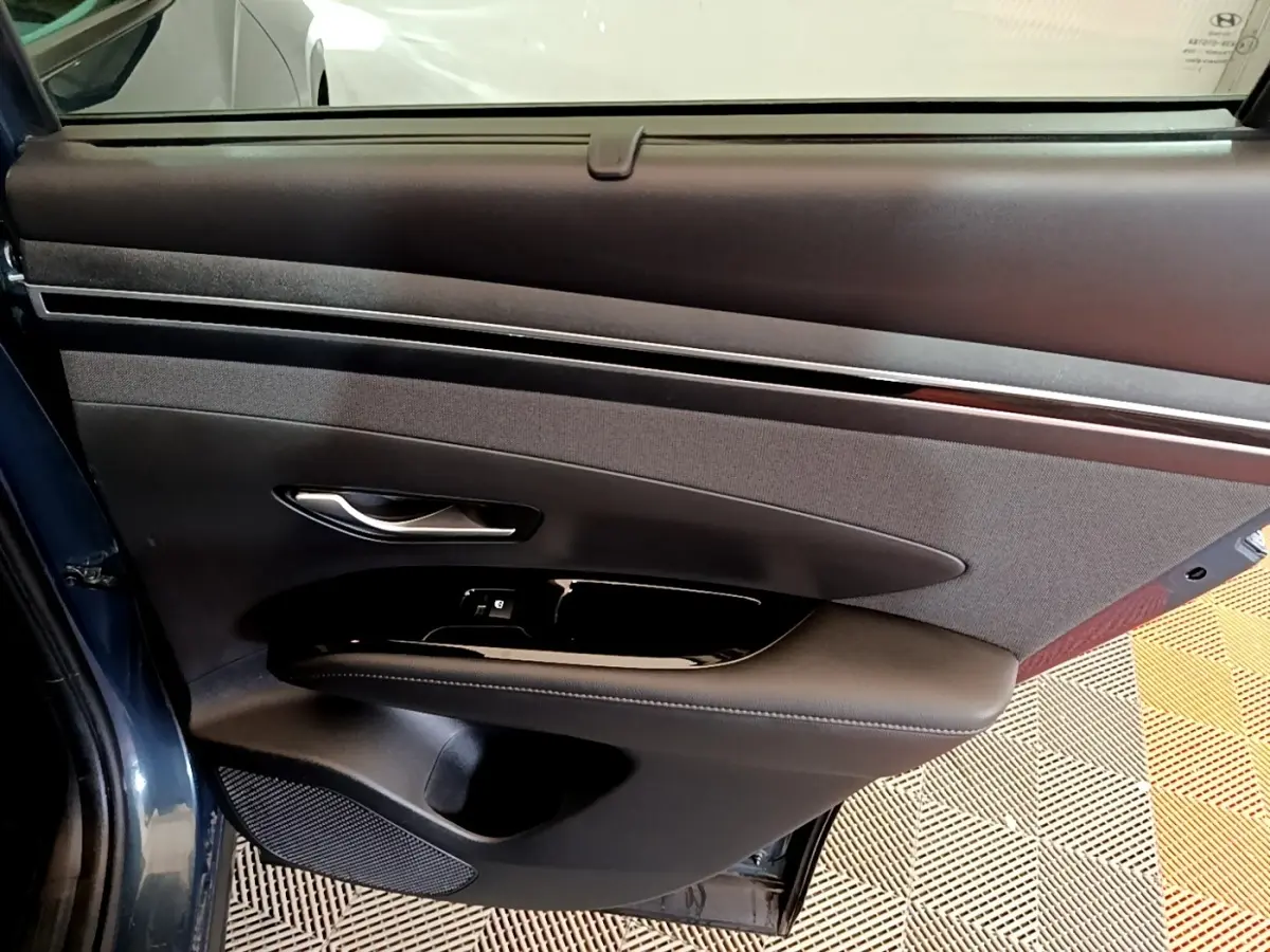 Vue intérieure de la porte arrière gauche bleu foncé du Hyundai Tucson 2023 avec garniture noire et commandes de fenêtre.