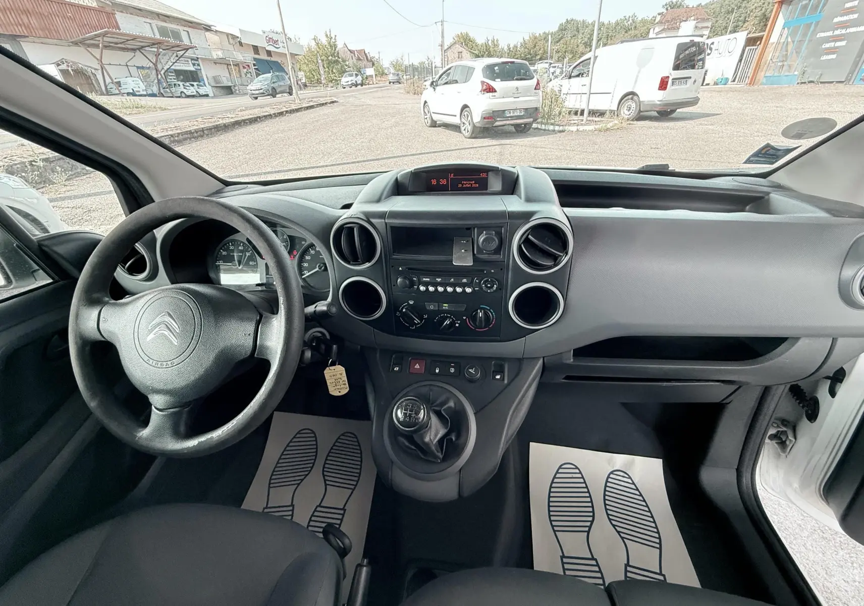 Vue intérieure du tableau de bord et volant côté gauche du Citroën Berlingo 2016 avec boîte manuelle et sellerie tissu noir.