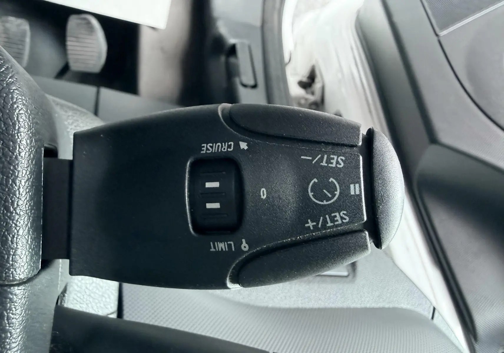 Gros plan sur la commande de régulateur de vitesse noire à gauche du volant dans l’habitacle d’un Citroën Berlingo blanc.