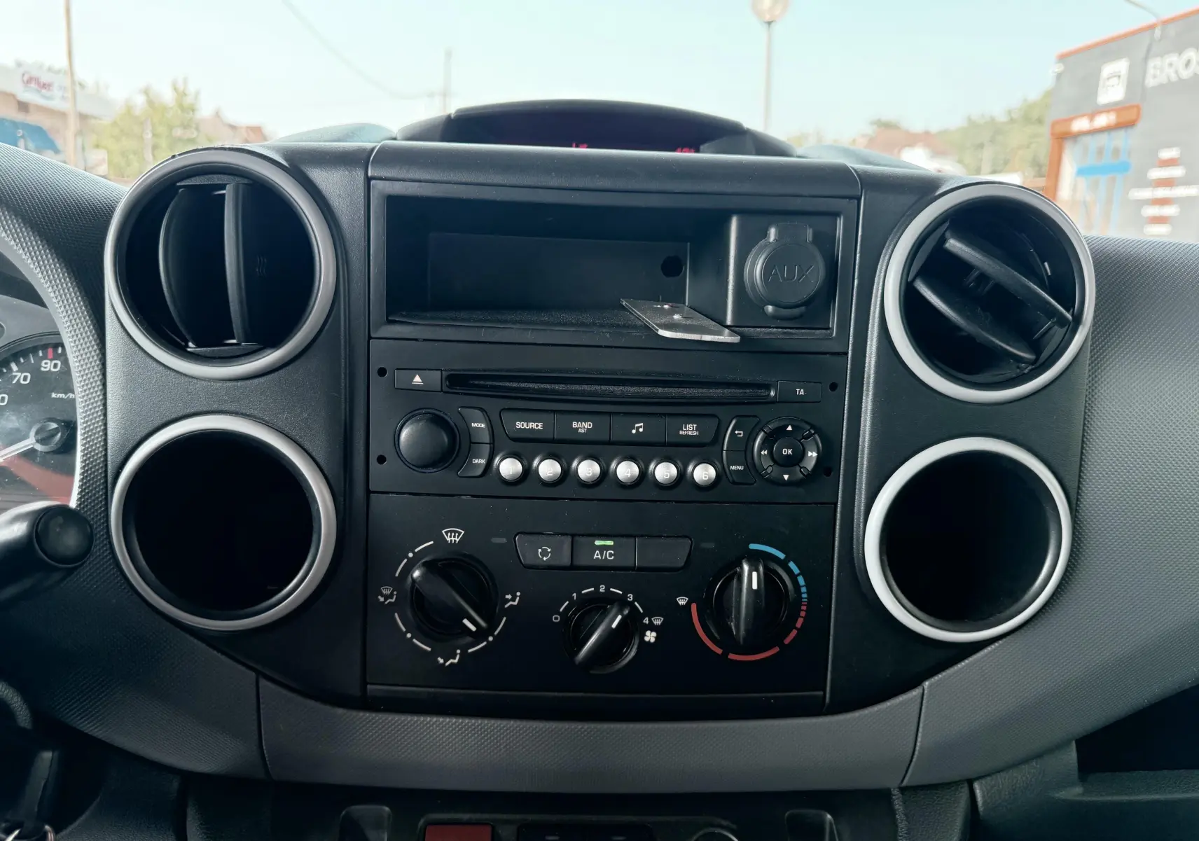 Tableau de bord central noir du Citroën Berlingo 2016 avec commandes de climatisation et lecteur audio, vue frontale rapprochée.