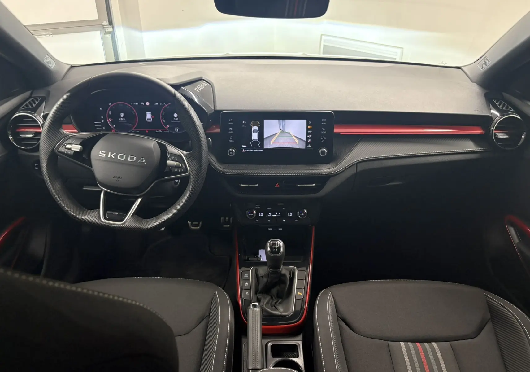 Vue intérieure avant de la Skoda Fabia Monte Carlo 2025, volant noir, détails rouges et écran central avec caméra de recul.
