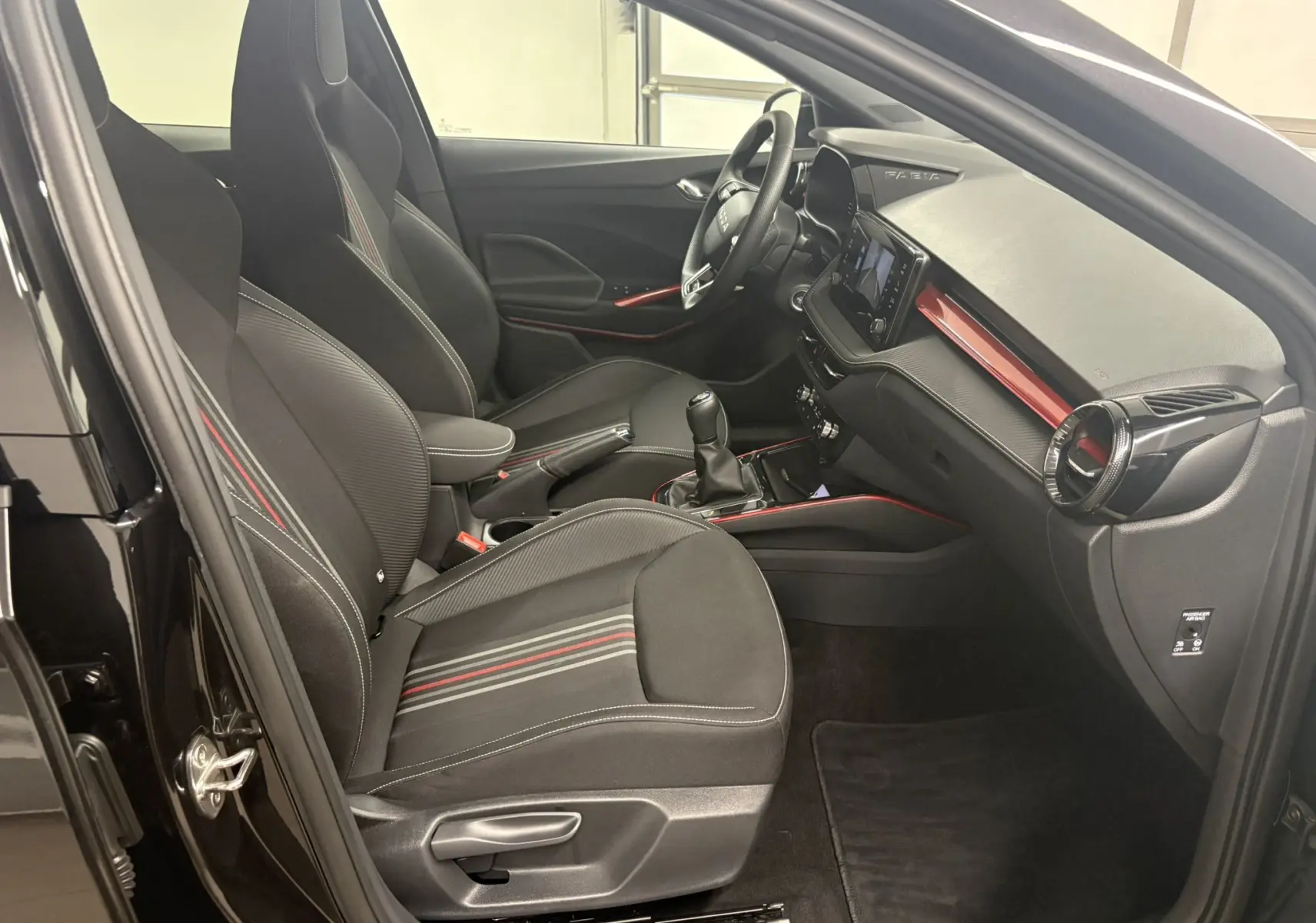 Intérieur de la Skoda Fabia Monte Carlo 2025 vu côté conducteur, sièges noirs avec surpiqûres rouges et tableau de bord assorti.