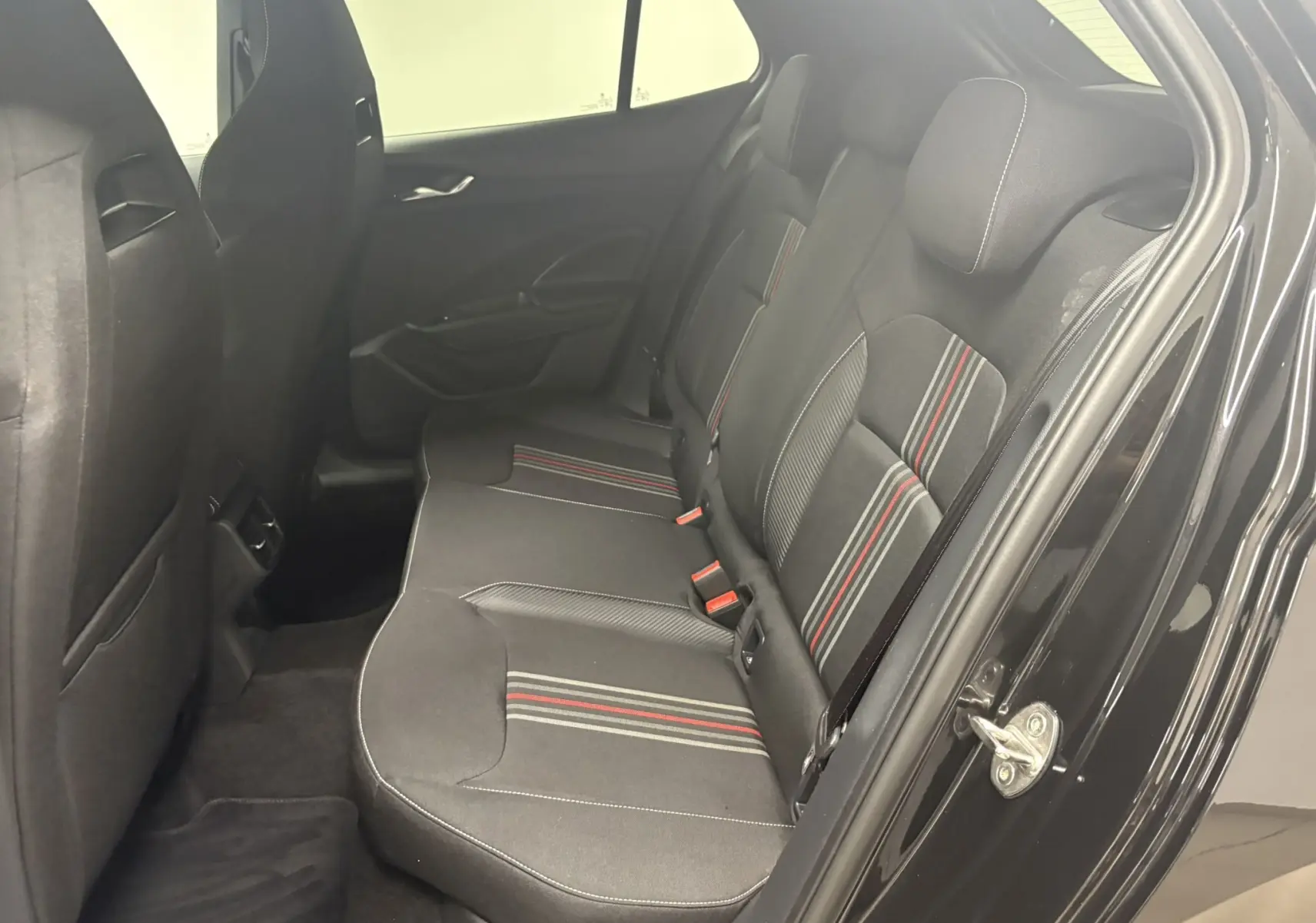 Vue intérieure côté arrière droit de la Skoda Fabia 2025 noire avec sièges tissu noirs à bandes rouges et grises.