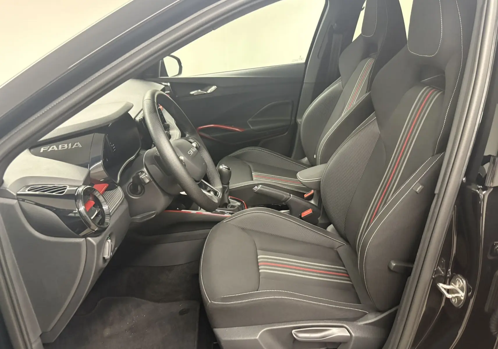 Vue intérieure côté conducteur de la Skoda Fabia Monte Carlo 2025 avec sièges noirs à bandes rouges et tableau de bord marqué Fabia.