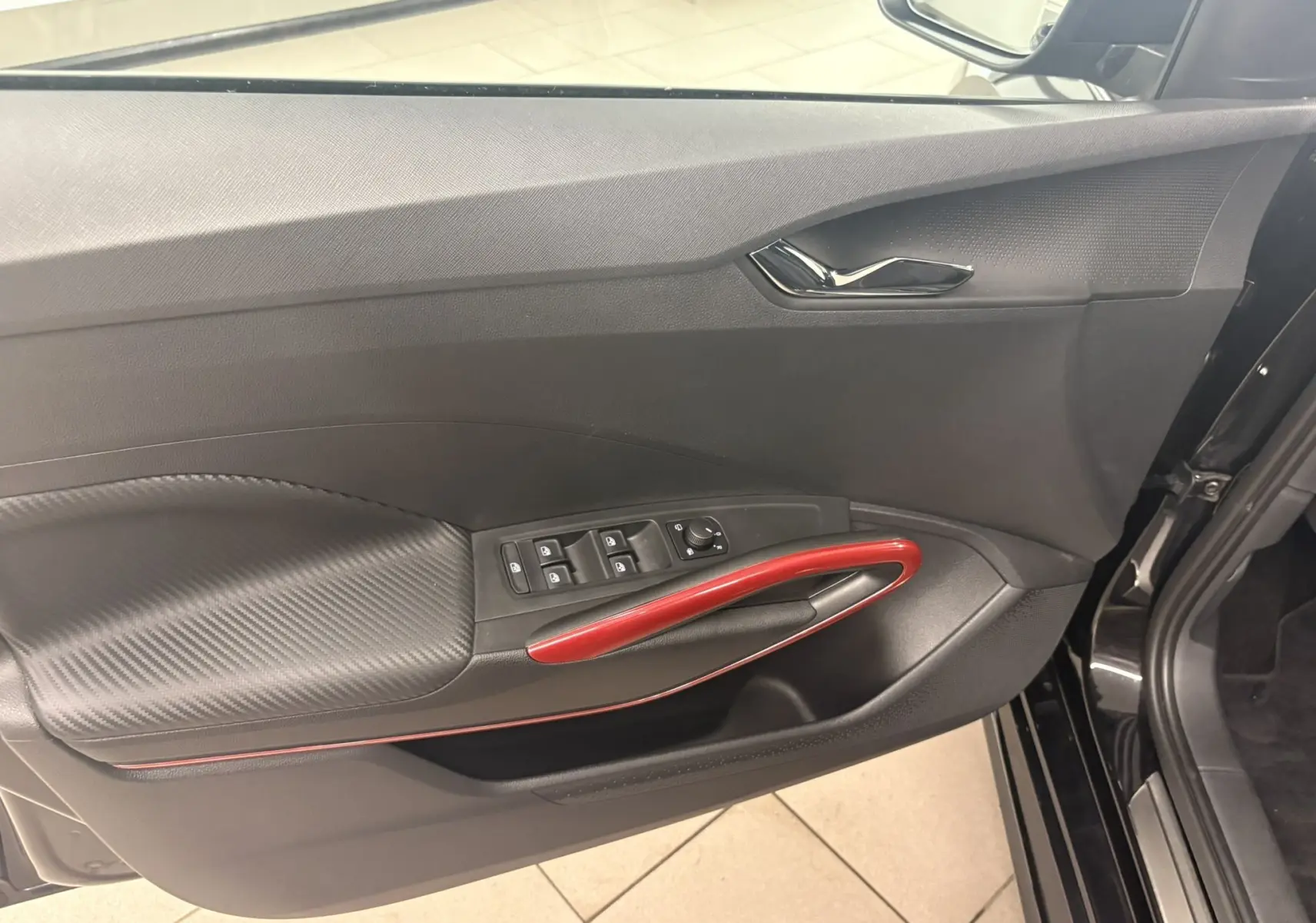 Vue intérieure de la porte avant gauche d'une Skoda Fabia 2025 noire avec poignée rouge et commandes de vitres.