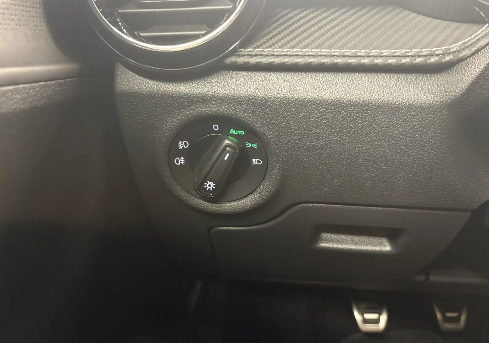 Gros plan sur le bouton de commande des phares à gauche du tableau de bord de la Skoda Fabia 2025 Noir Magic nacré.
